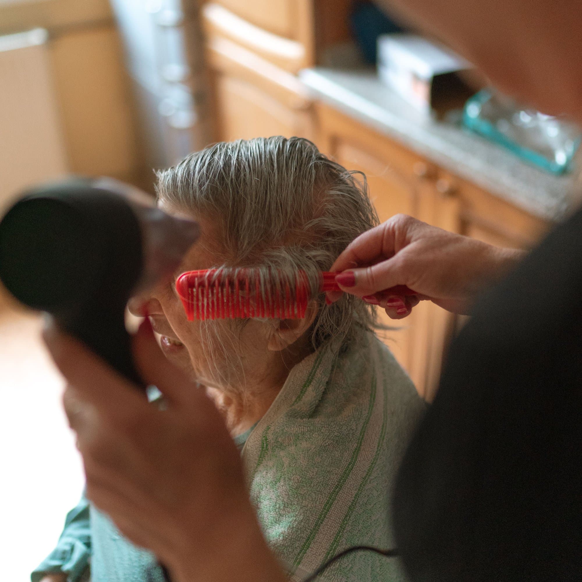 A caregiver styling an older woman's hair at home.