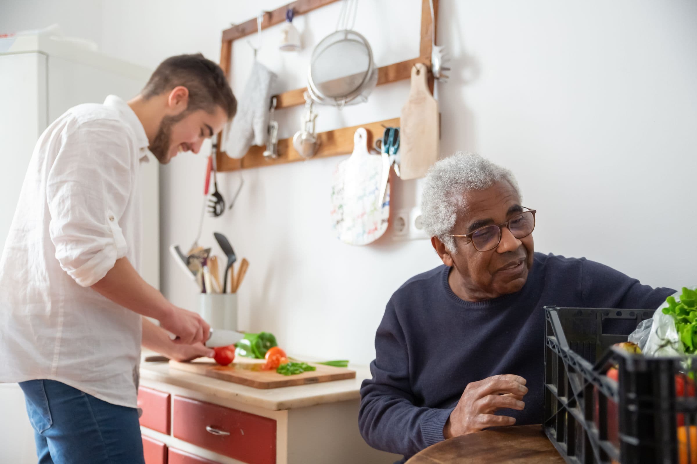 A caregiver and an older man preparing vegetables together in a kitchen.
