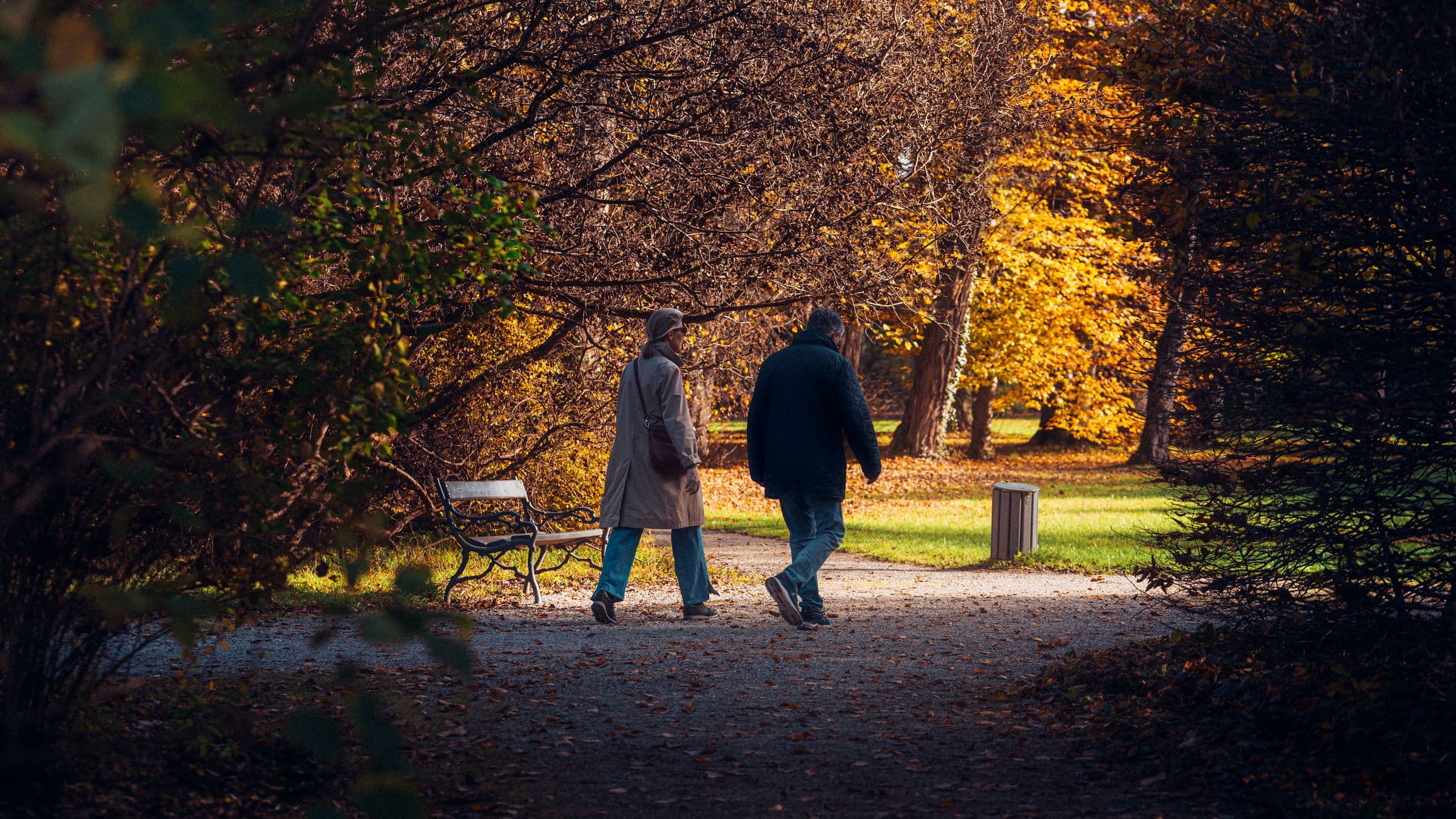 An older couple walking together through a park in autumn.