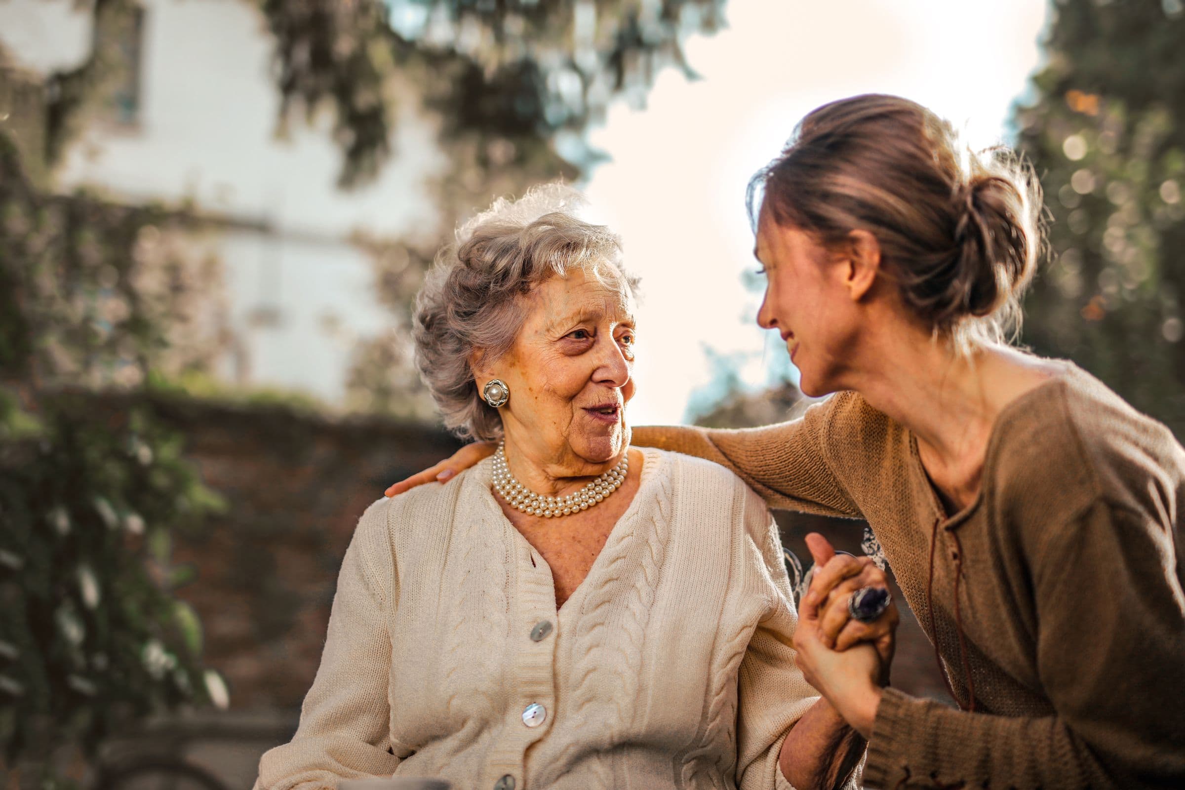 An adult daughter greeting her mother with a hug in the garden.